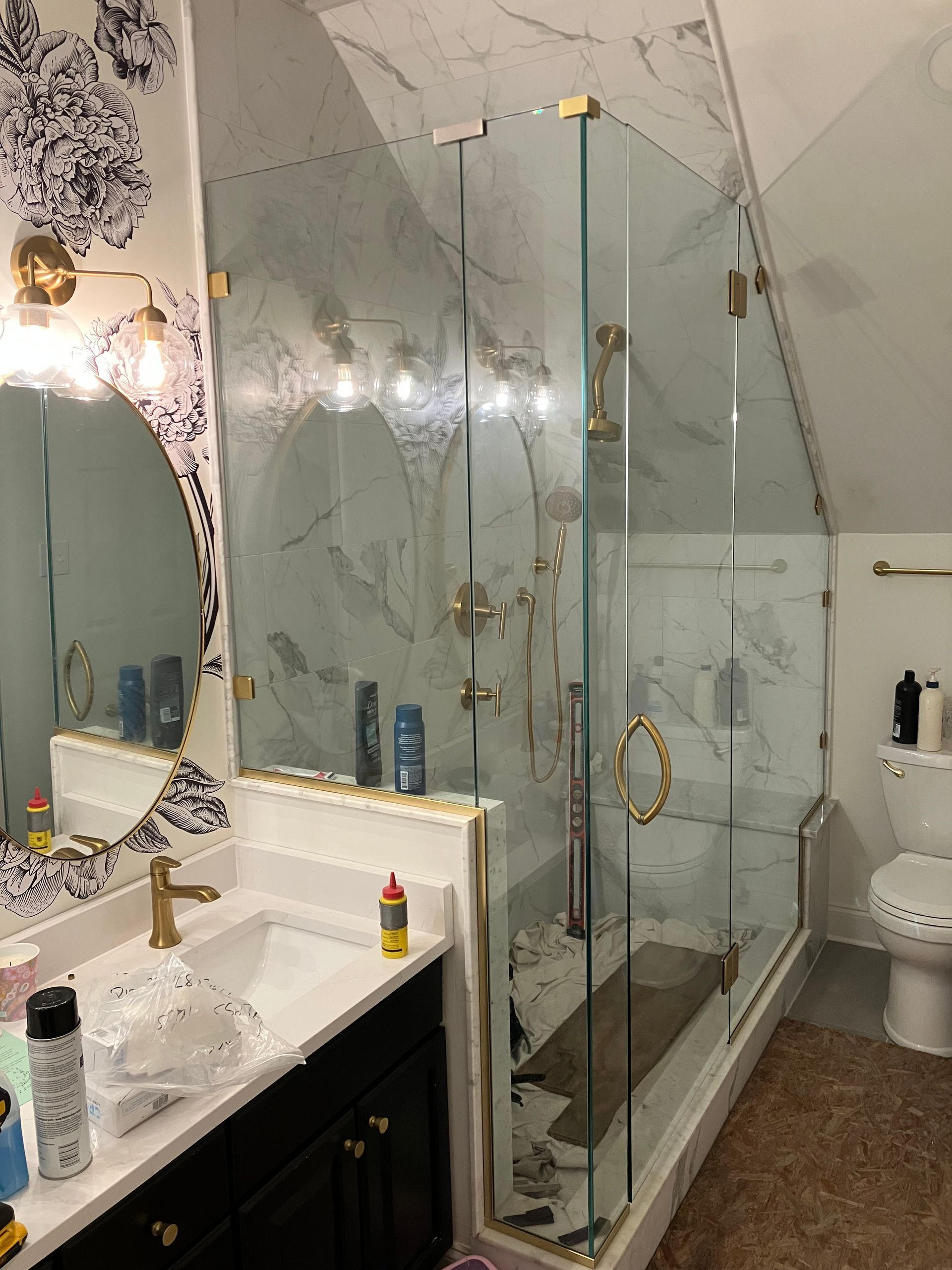 A bathroom vanity with a patterned backsplash and a walk-in glass shower enclosure next to a toilet in a marble-tiled room.