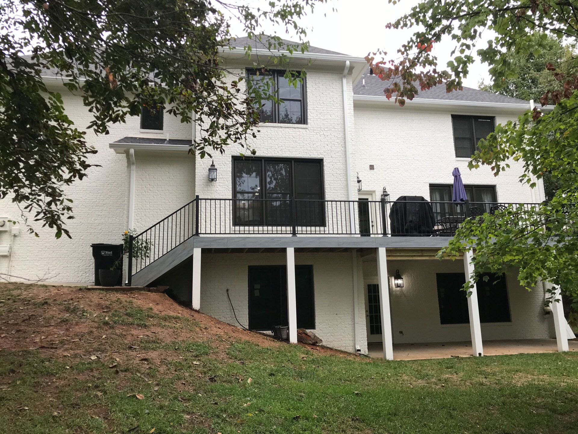 A white, two-story house with a rear deck, dark-framed windows, and a partially shaded lawn.
