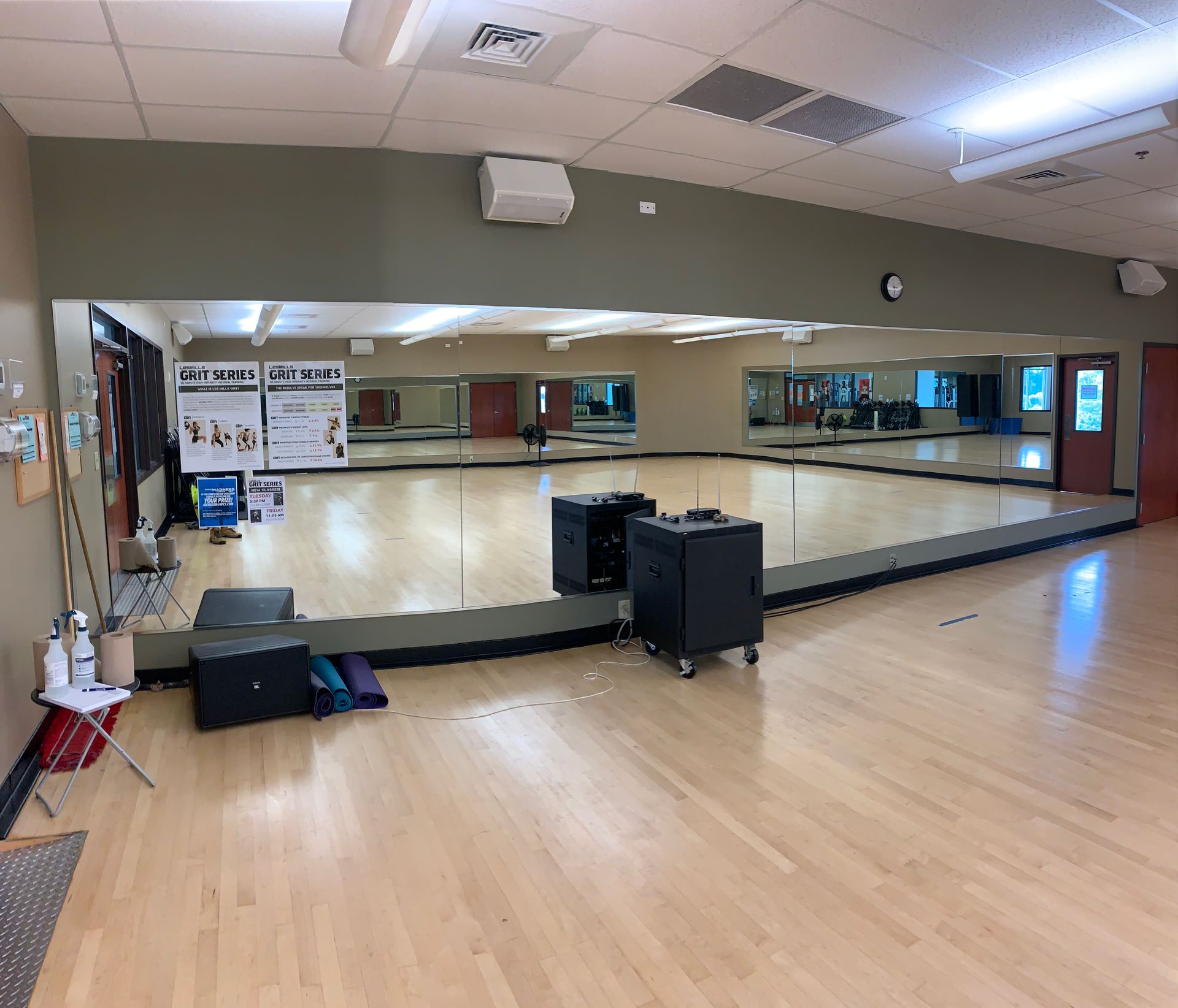 Empty dance studio featuring a wall of floor-to-ceiling mirrors, light wood floors, and some equipment near the walls.