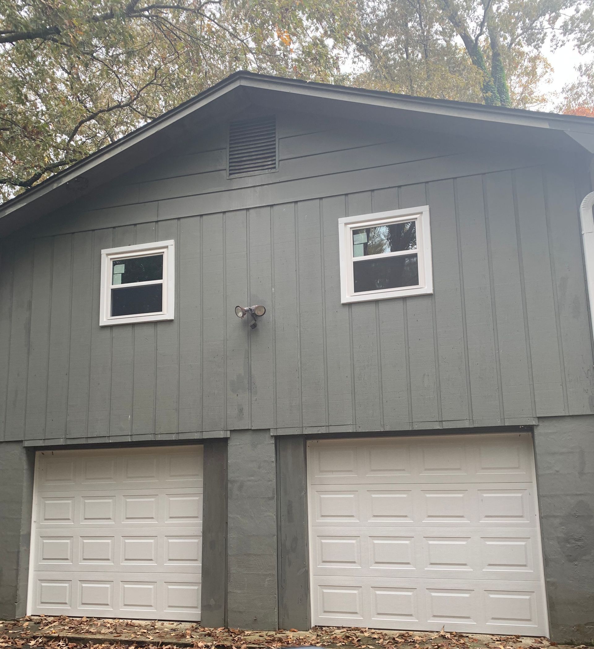 A grey two-story garage with two white bay doors on the lower level and two white windows on the upper level.
