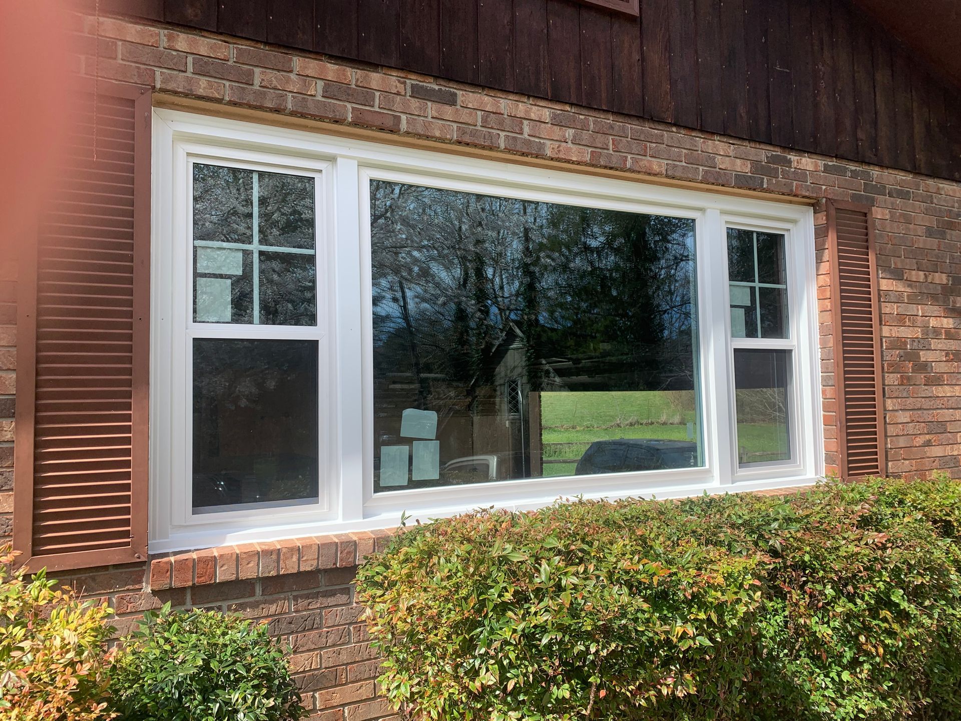 A large, white-framed window with a center picture pane and two flanking operable windows set in a brick exterior wall.