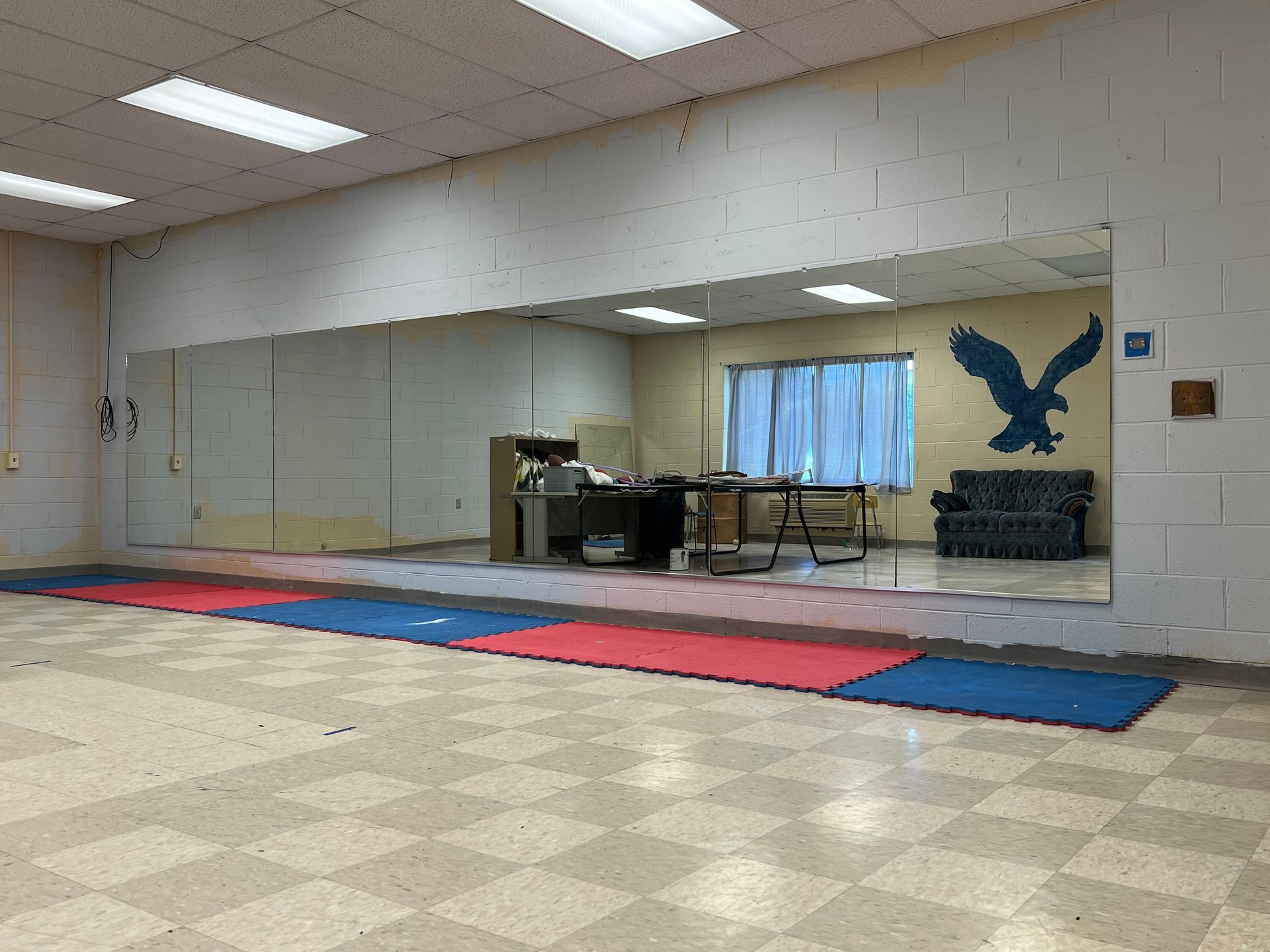 A brightly lit fitness room with mirrored walls, a checkerboard floor, and colorful exercise mats lined up.