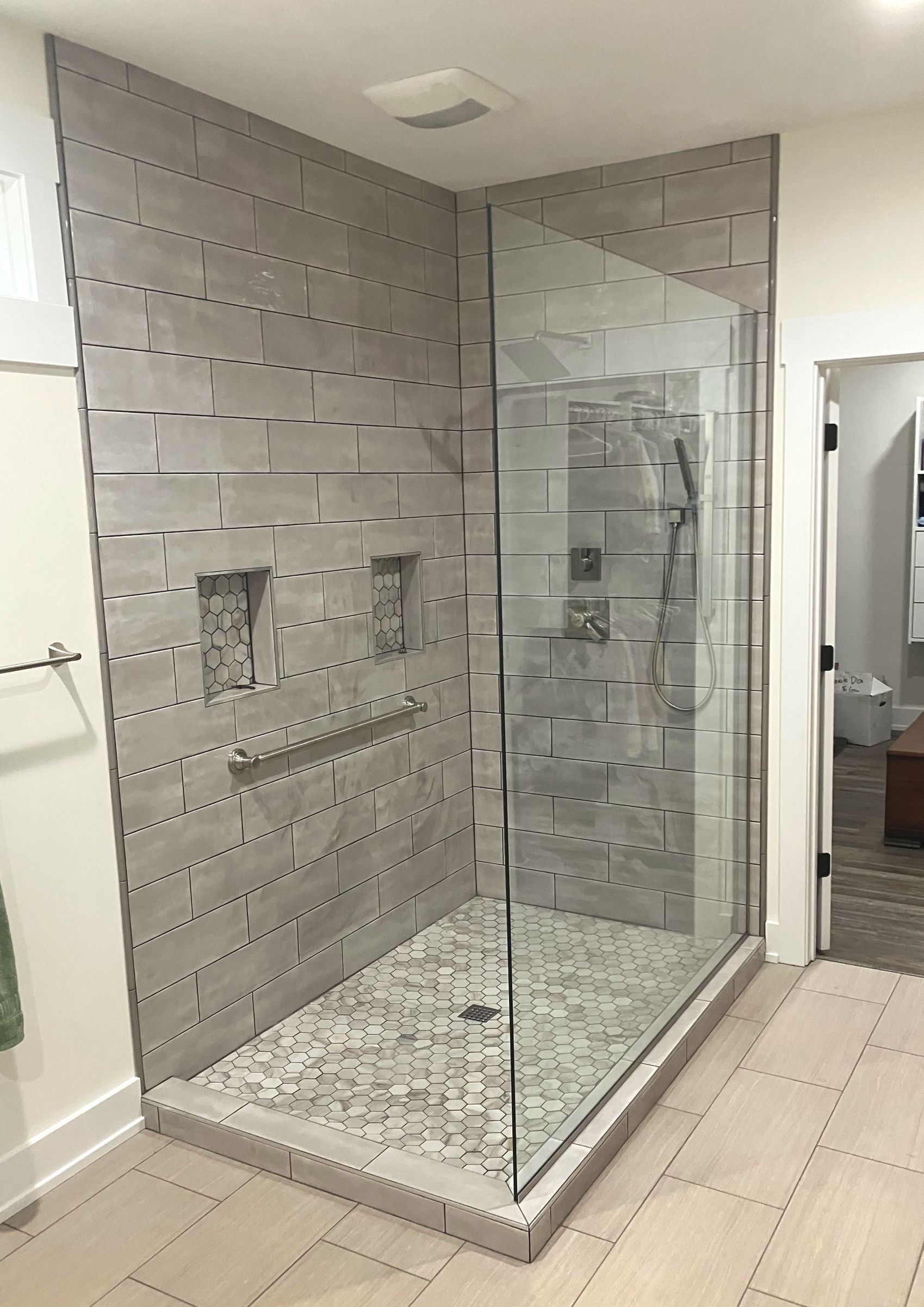 Modern walk-in shower with light grey tiled walls, patterned tile floor, glass door, and built-in wall niches.