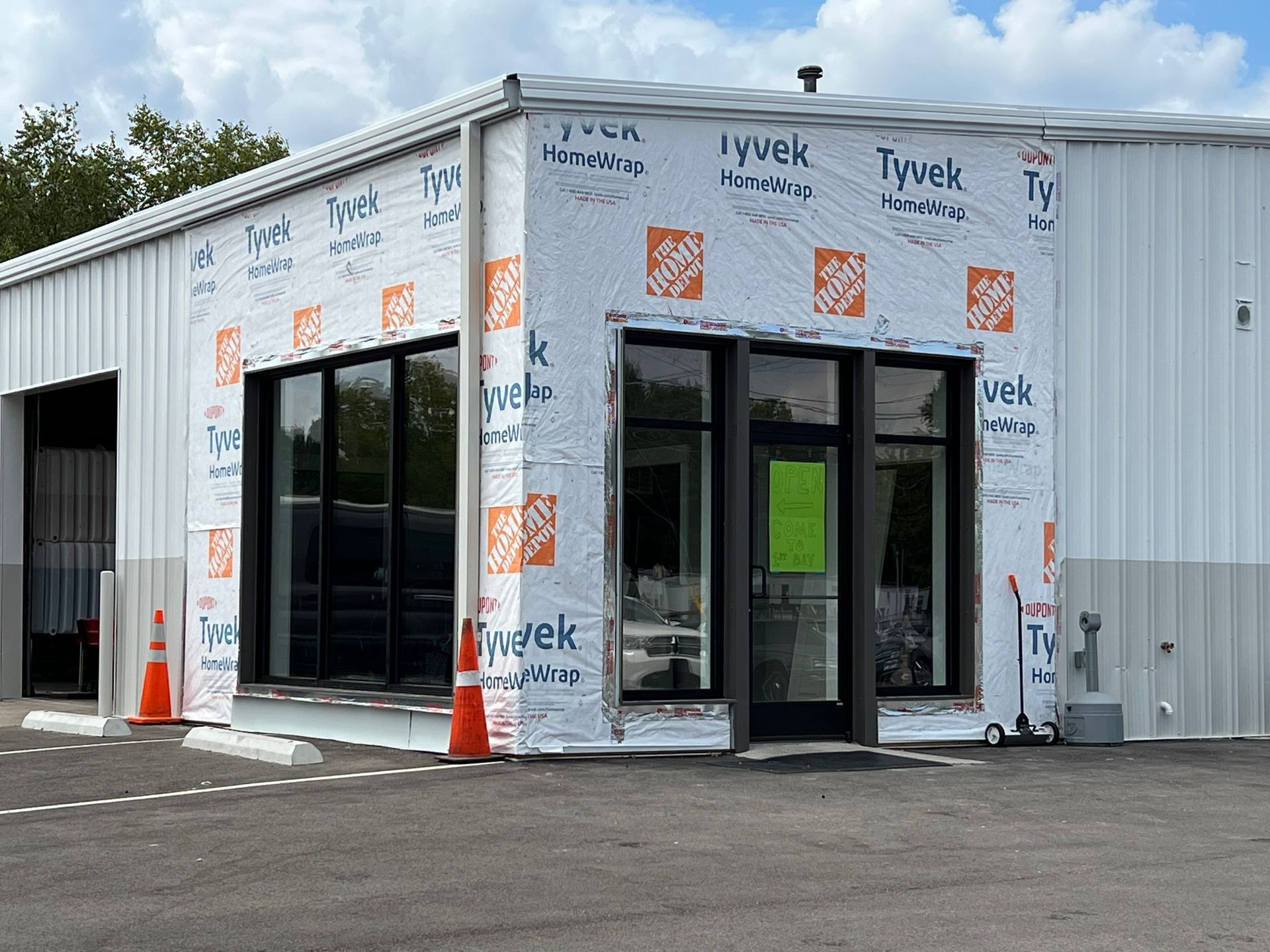A commercial building under construction with white metal siding and Tyvek house wrap on the exterior walls and storefront.