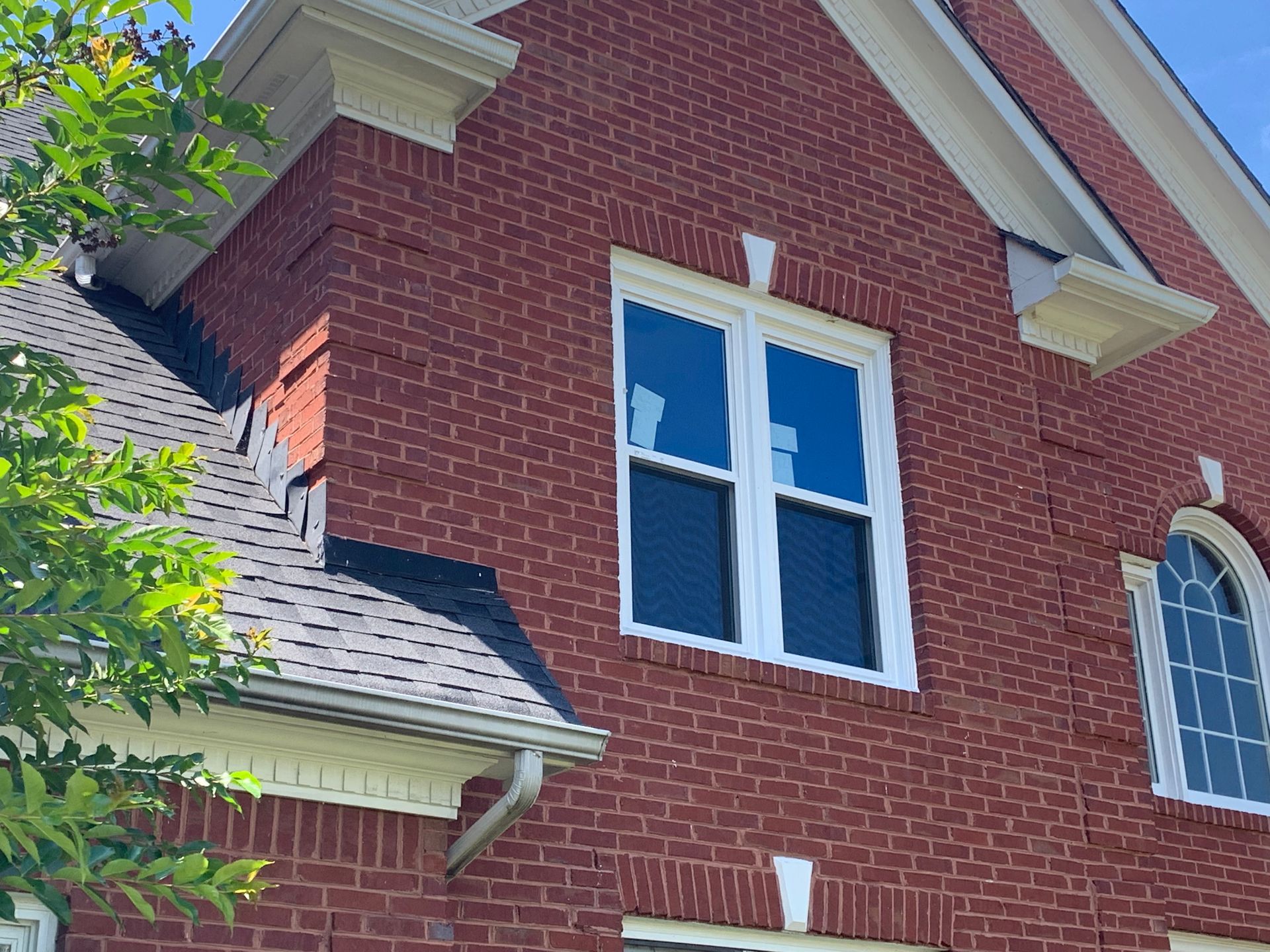 A two-story red brick house exterior featuring a white-framed rectangular window and an arched window under a gabled roof.
