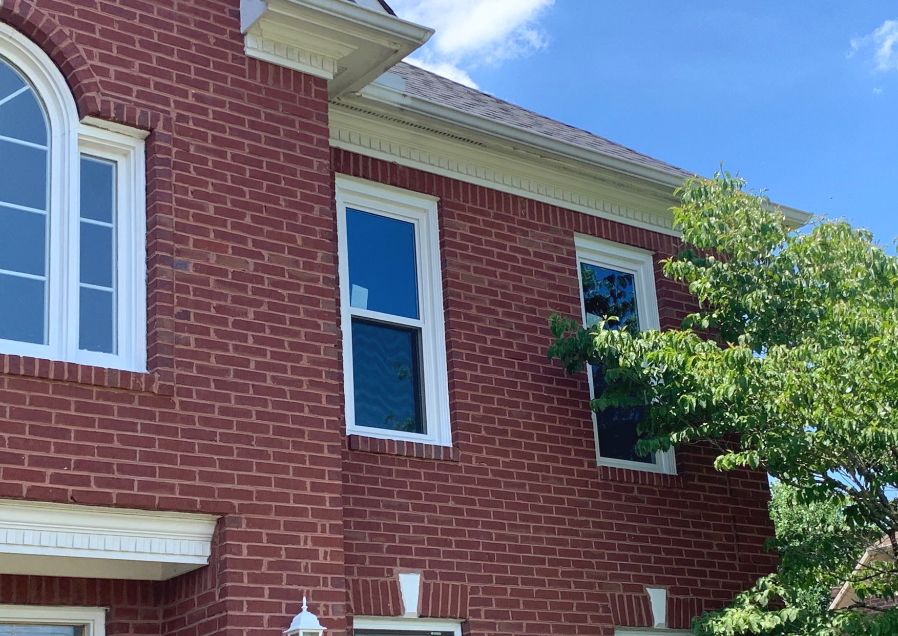 A red brick house exterior showing a multi-paned arched window and two standard rectangular windows under the roofline.