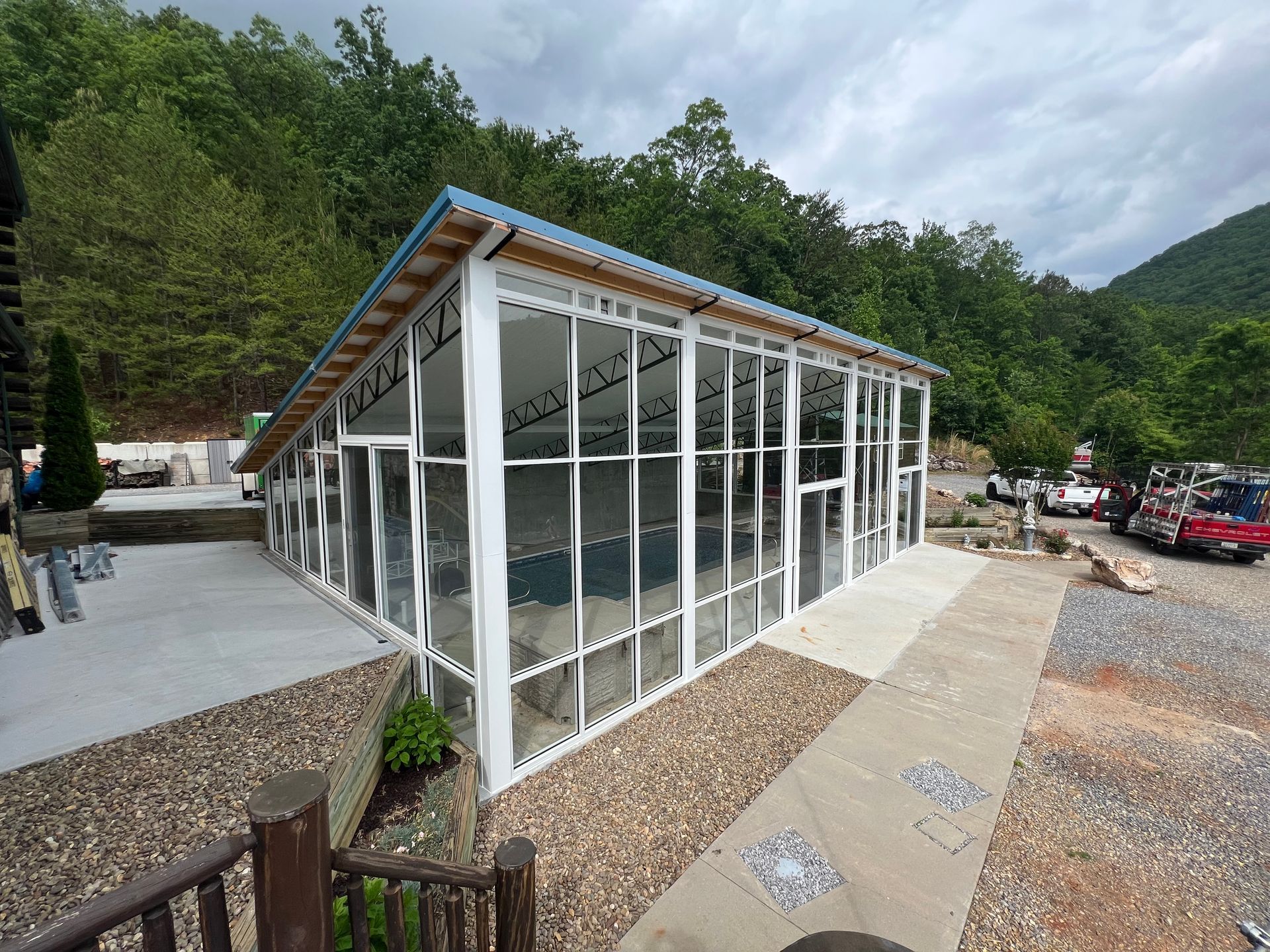 A modern white pool enclosure with glass walls and a sloped roof set against a mountain landscape.