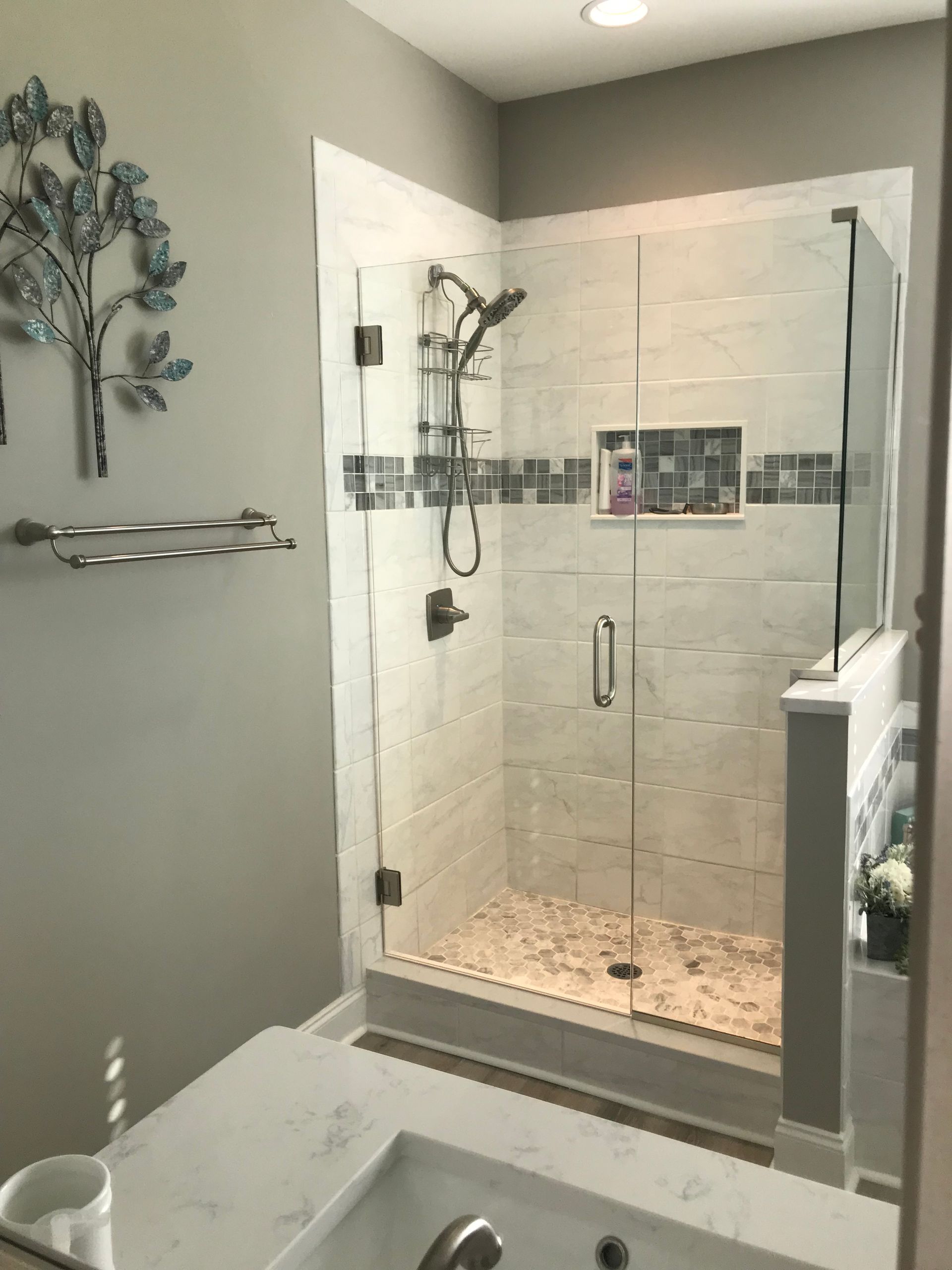 Modern bathroom featuring a tiled walk-in shower with a glass door, a stone-pebble floor, and a marble vanity countertop.