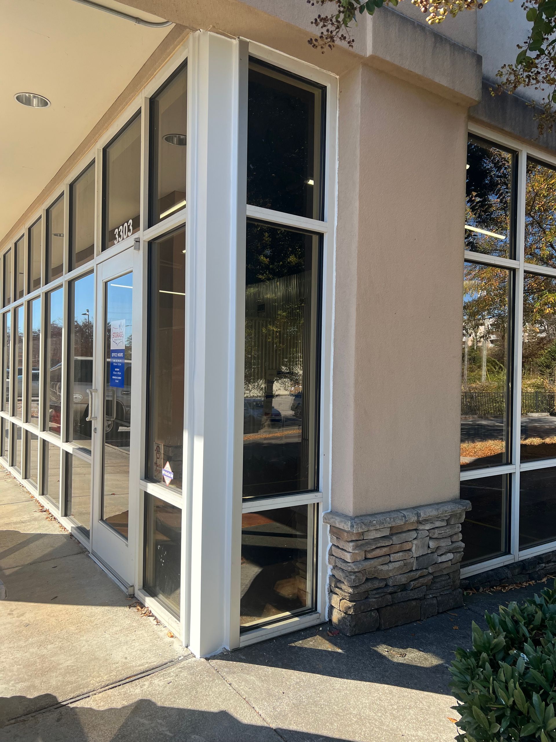 A commercial building corner with glass walls, a white-framed entrance door, and a stone-accented exterior column.