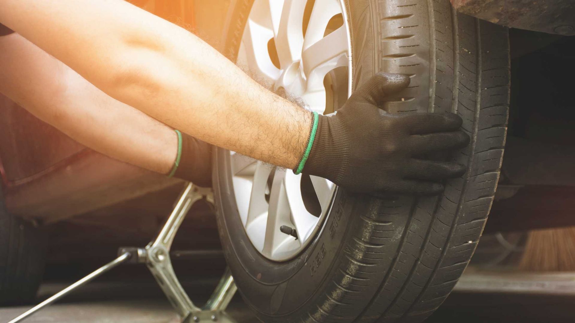 Gloved hands changing a car tire with a jack near the wheel