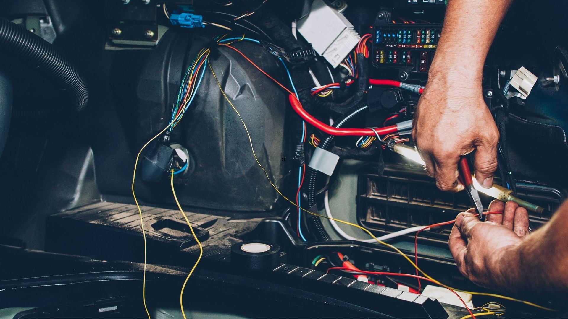 Hands wiring a car dashboard with exposed red and yellow cables and electronic components