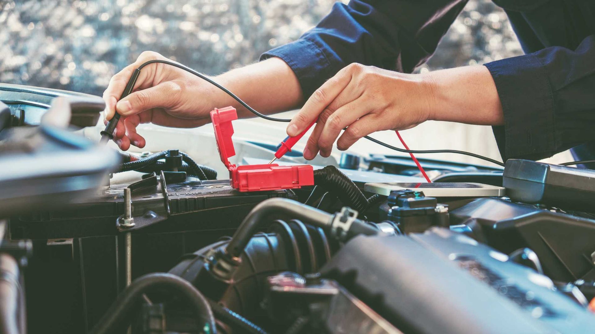 Hands testing car battery with jumper cables in an engine bay