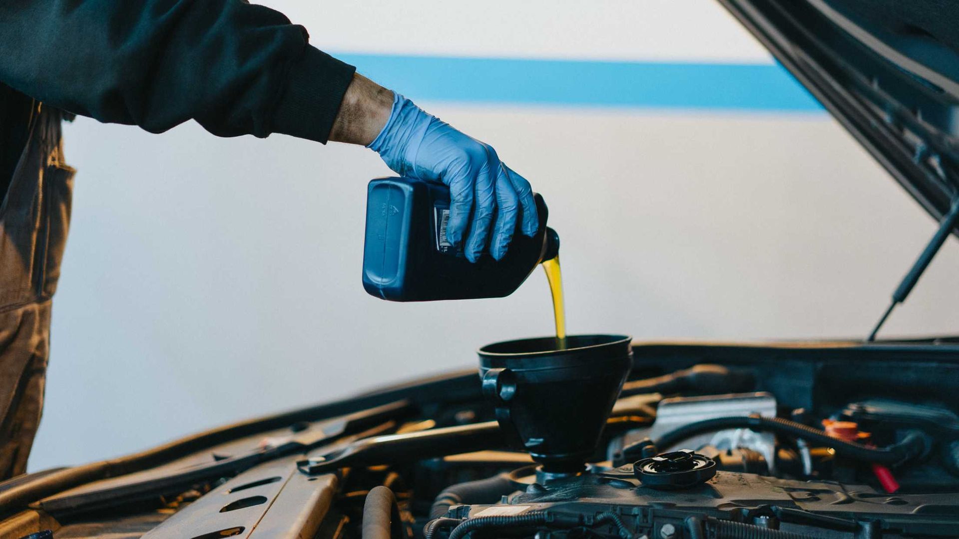Mechanic pouring engine oil into a car’s open engine bay from a bottle