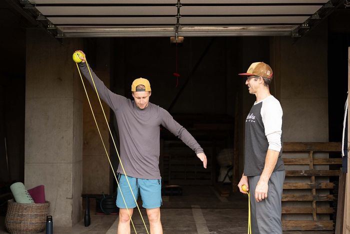 Two men are measuring a ball with a tape measure in a garage.