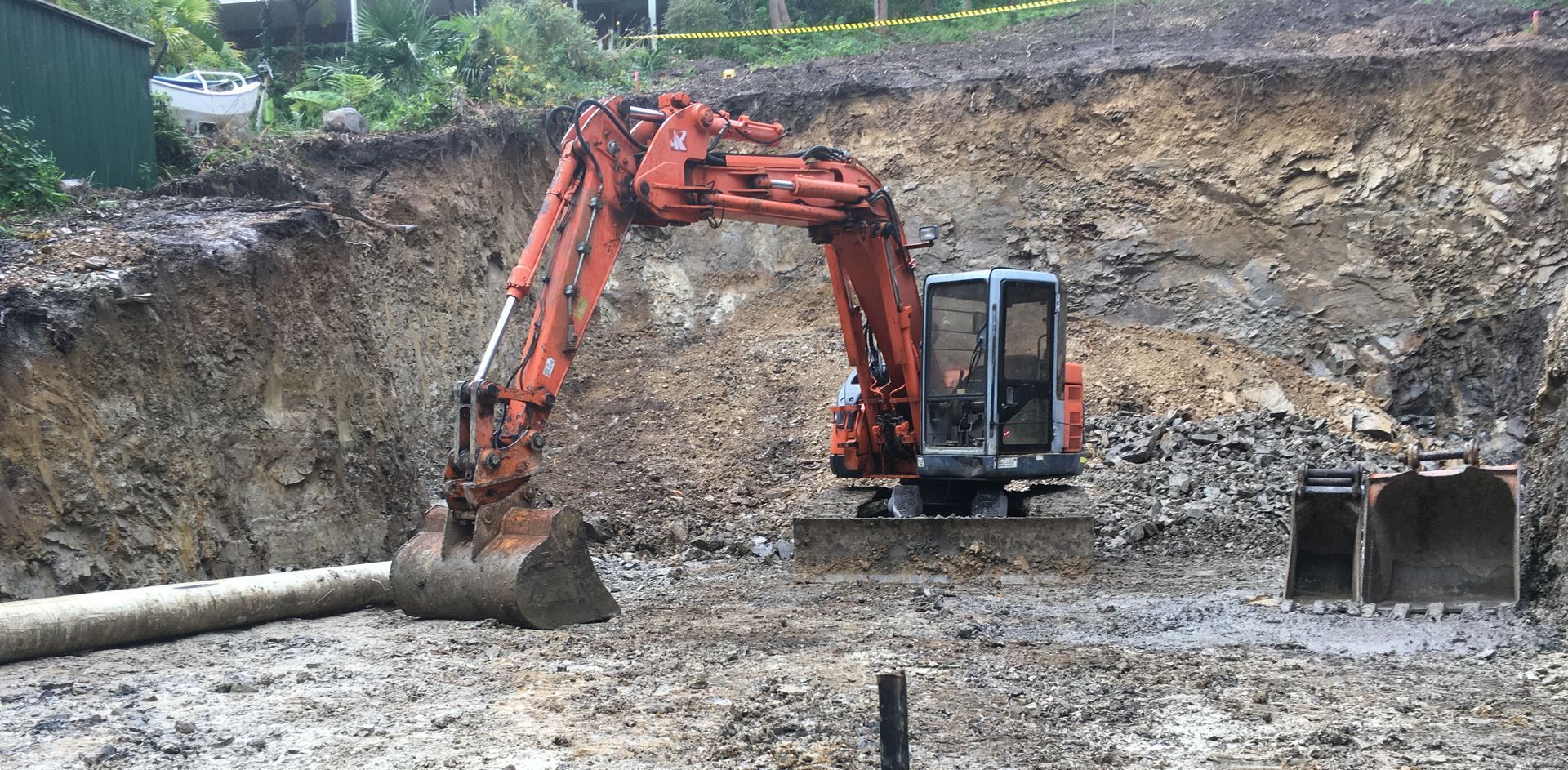An orange excavator digs into a muddy pit. A pipe lies on the ground. — Lakesway Earthmoving in Charlotte Bay, NSW