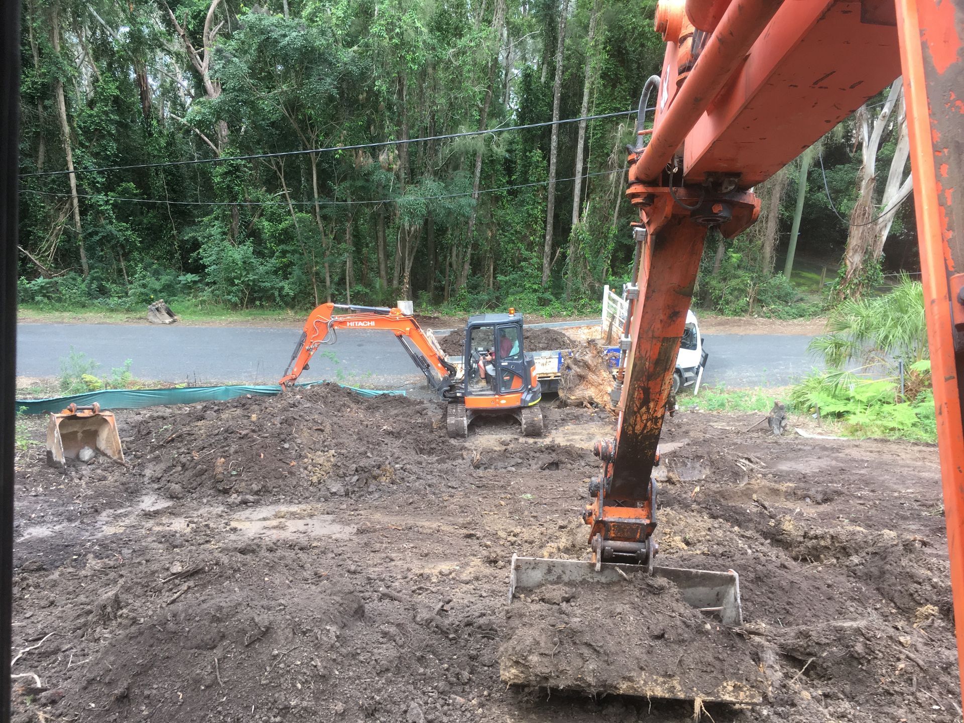 Construction site: orange excavator scoops dirt, another in background. Road and trees visible. — Lakesway Earthmoving in Charlotte Bay, NSW