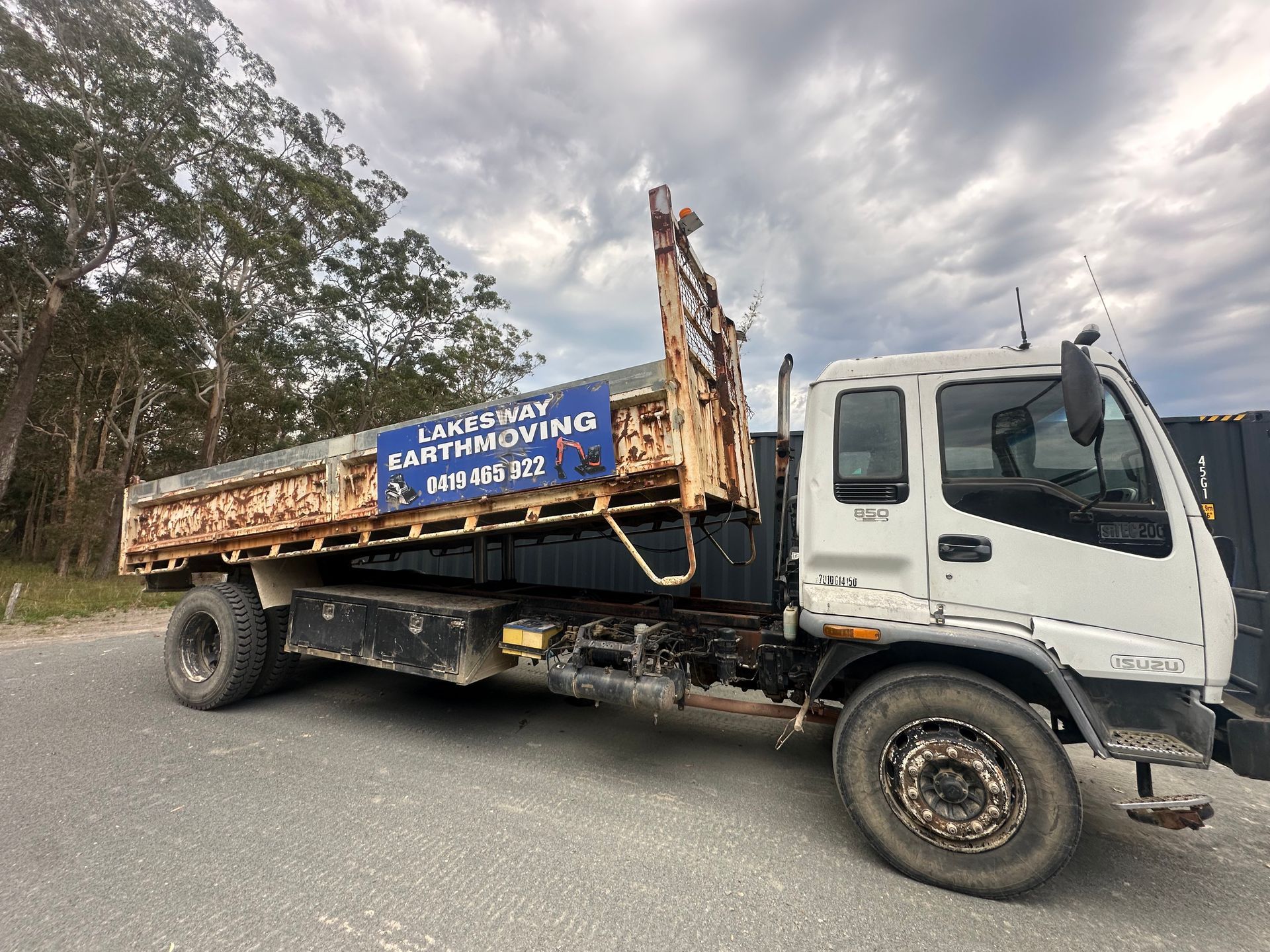 White Isuzu flatbed truck, side view, outdoors, cloudy sky. — Lakesway Earthmoving in Charlotte Bay, NSW