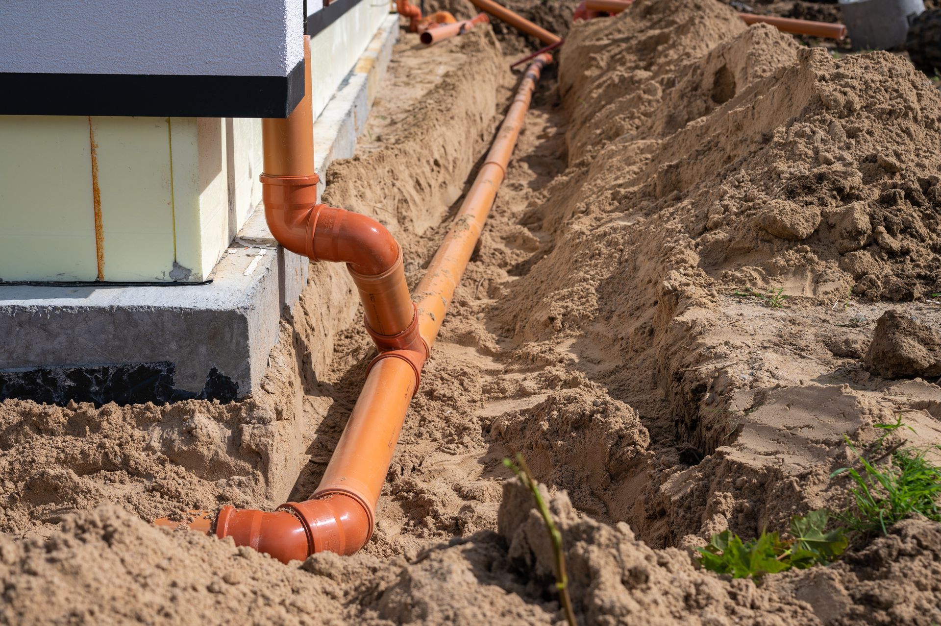 Orange drainage pipes installed in a trench next to a building foundation in sand. Orange drainage pipes installed in a trench next to a building foundation in sand.
