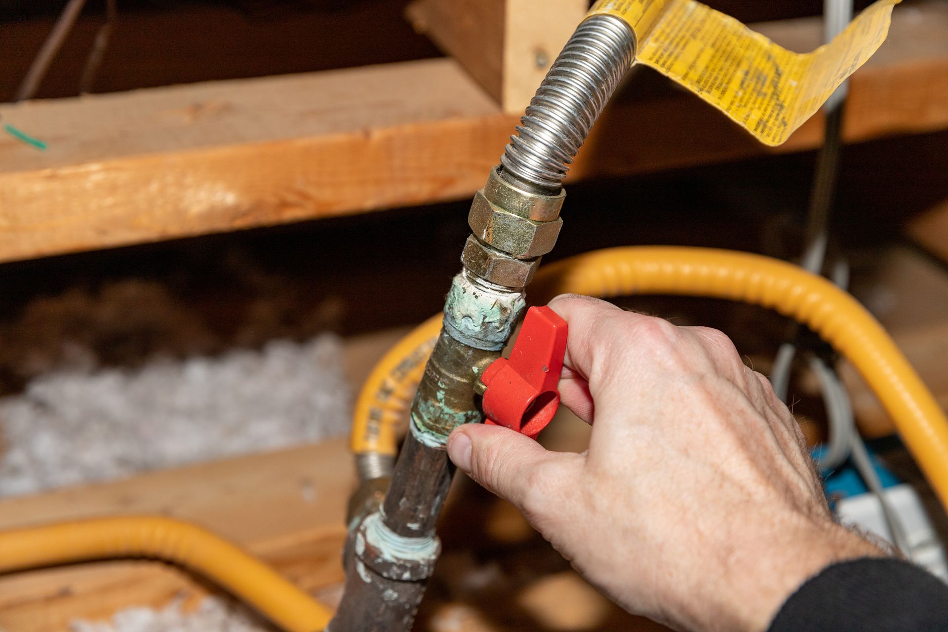 Hand turning a red gas shut-off valve on a corroded pipe in an attic setting. Hand turning a red gas shut-off valve on a corroded pipe in an attic setting.