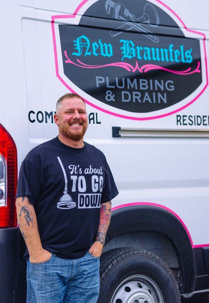 Man pointing at pipes under a sink, explaining to a woman who watches, another person at left.
