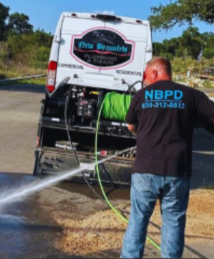 Plumber working on copper pipes with a wrench and valve, inside. Worker pressure-washing the back of a white service van on a sunny roadside