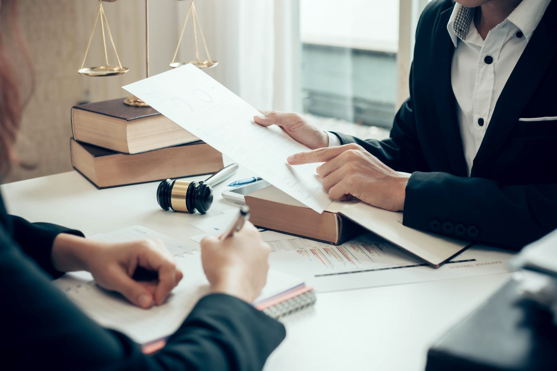 Two people reviewing legal documents at a desk with gavel and scales. Two people reviewing legal documents at a desk with gavel and scales.