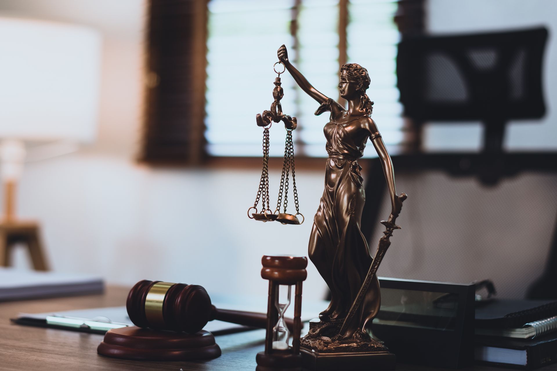 A Lady Justice statue stands beside a gavel and hourglass on a law office desk.