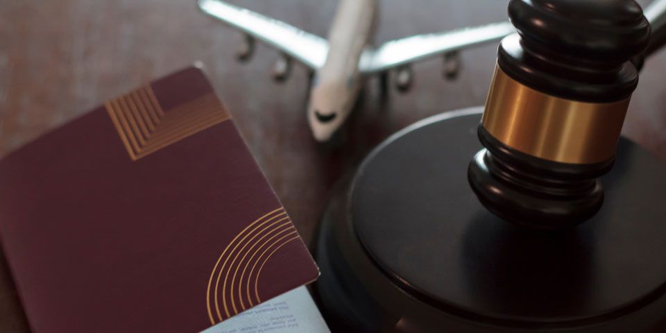 Auf einem Holztisch liegt neben einem Reisepass und einem Flugzeug ein Richterhammer.