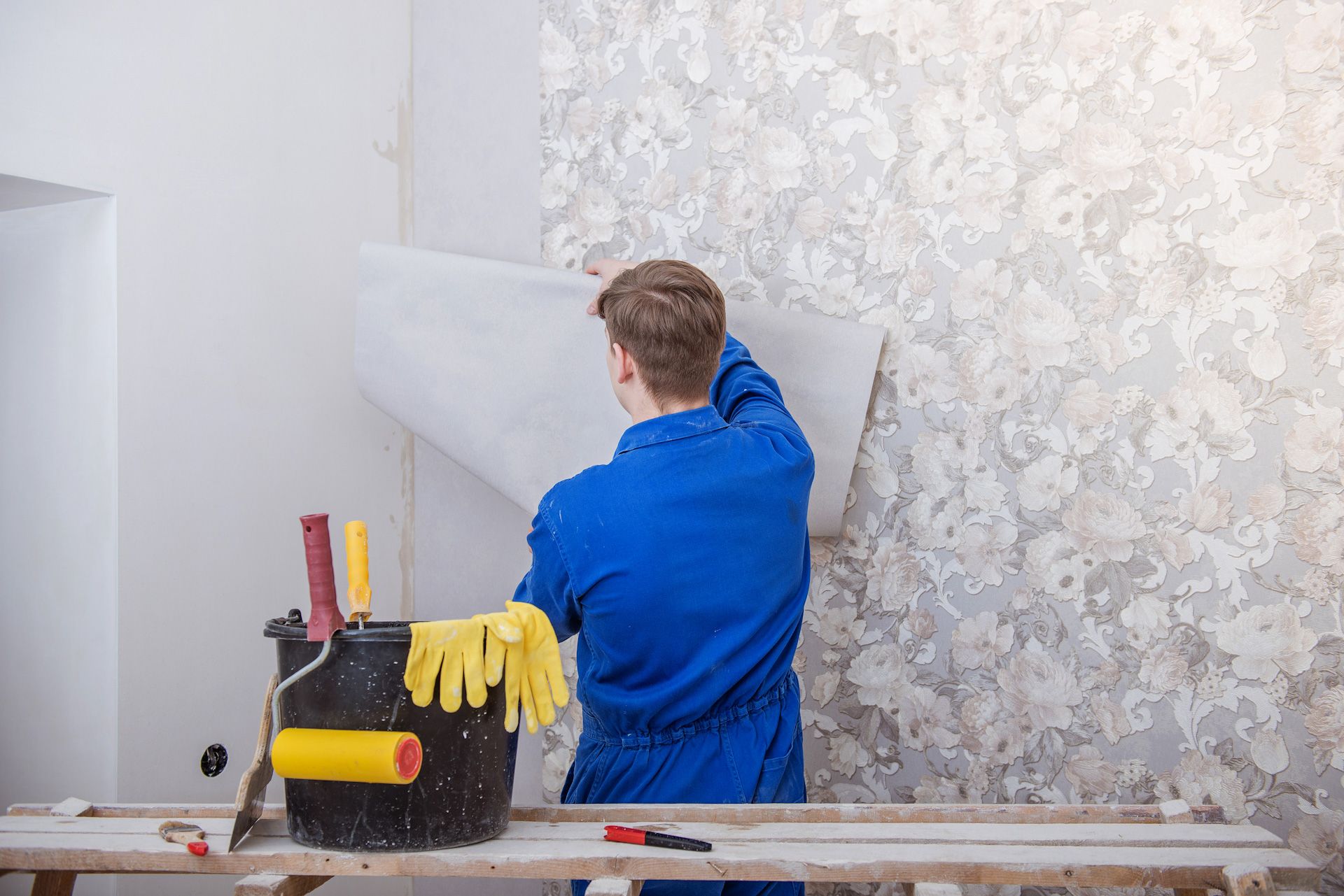 A man is removing wallpaper from a wall.