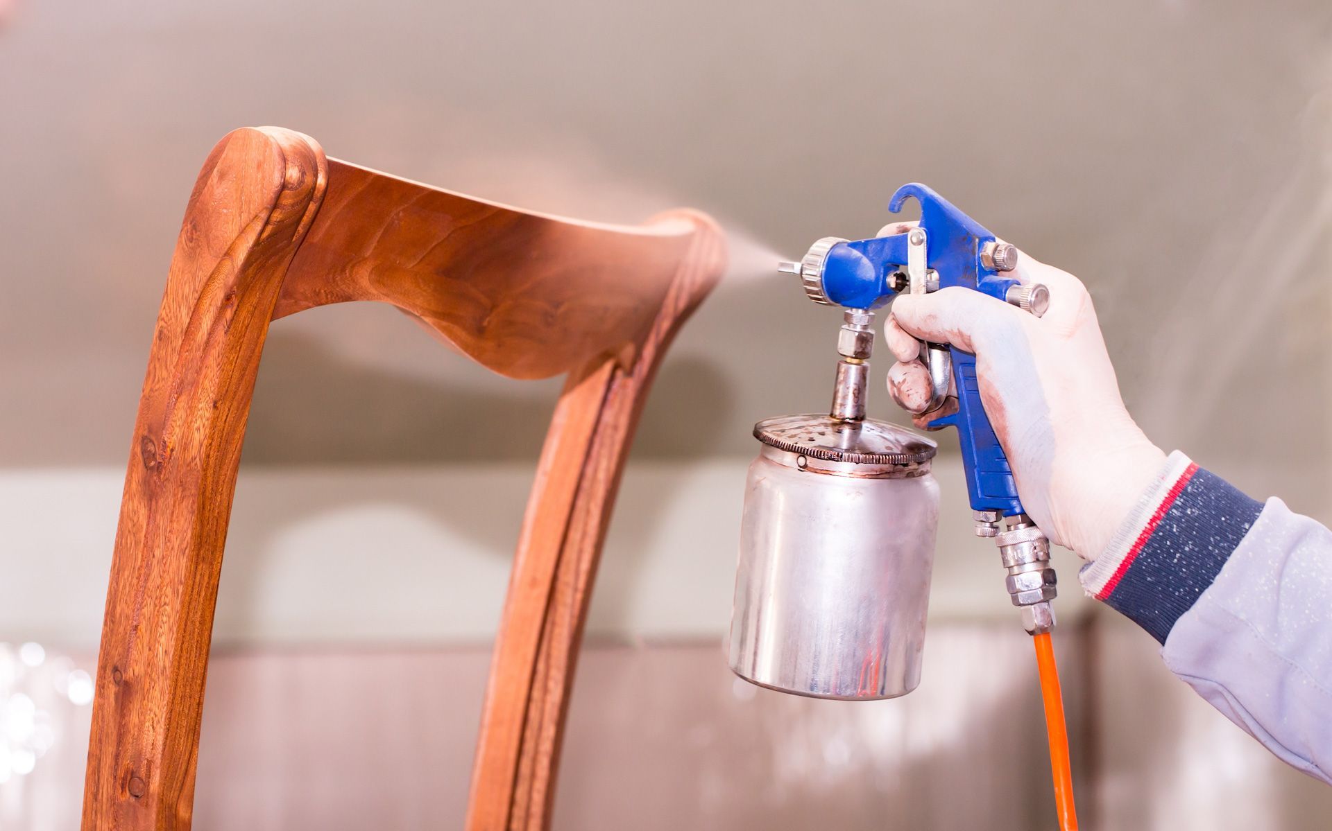 A person is spraying paint on a wooden chair.