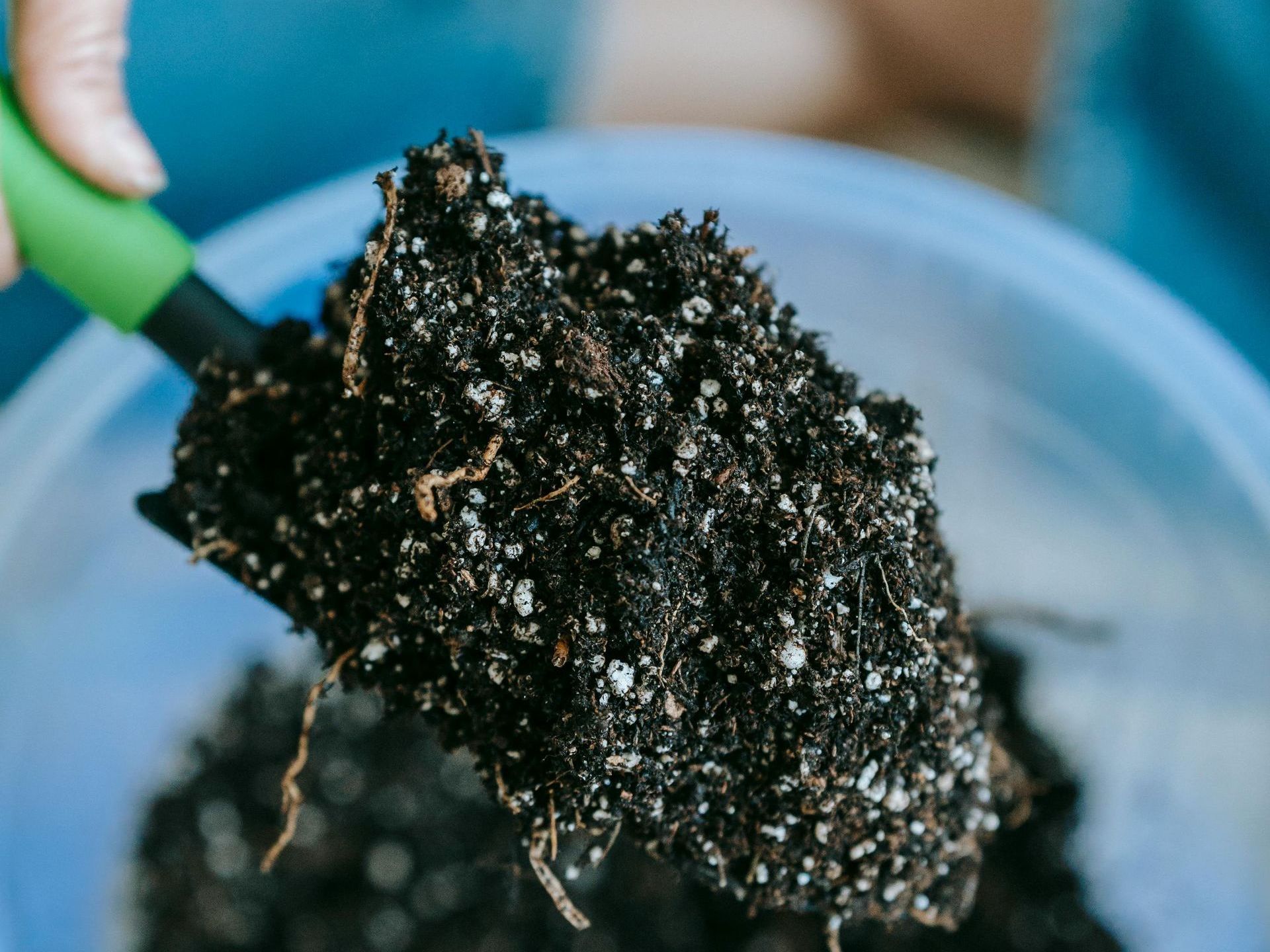 organic plant fertilizer A person is holding a shovel over a bowl of soil.