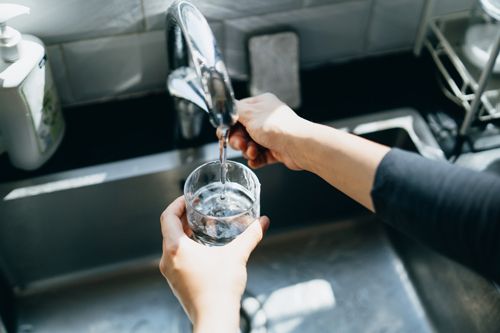 A Person Is Pouring Water From A Faucet Into A Glass - Fort Worth, TX - Andress Plumbing