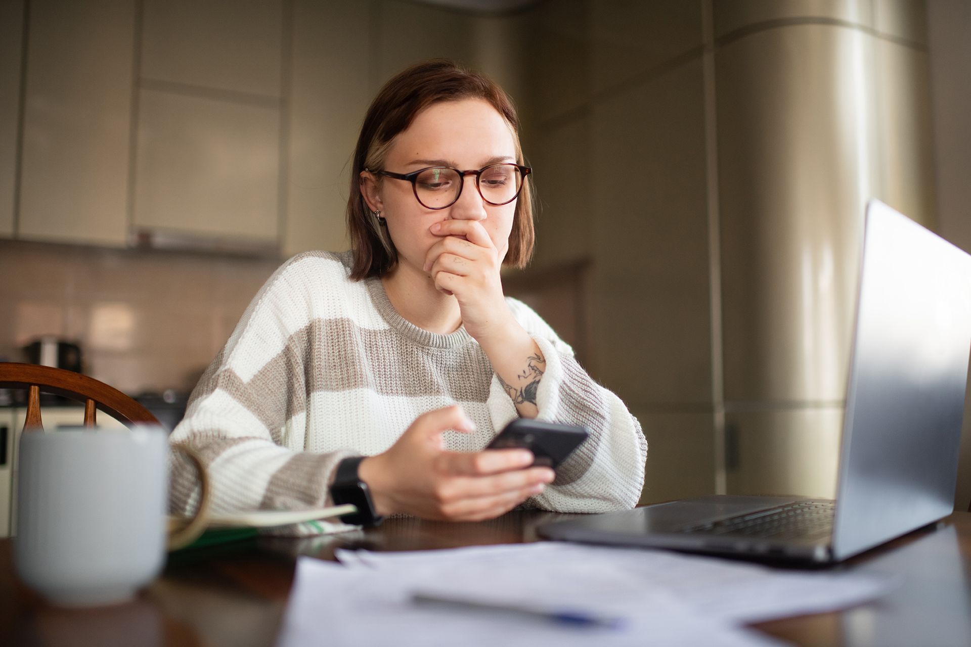 A woman is sitting at a table with a laptop and a cell phone.