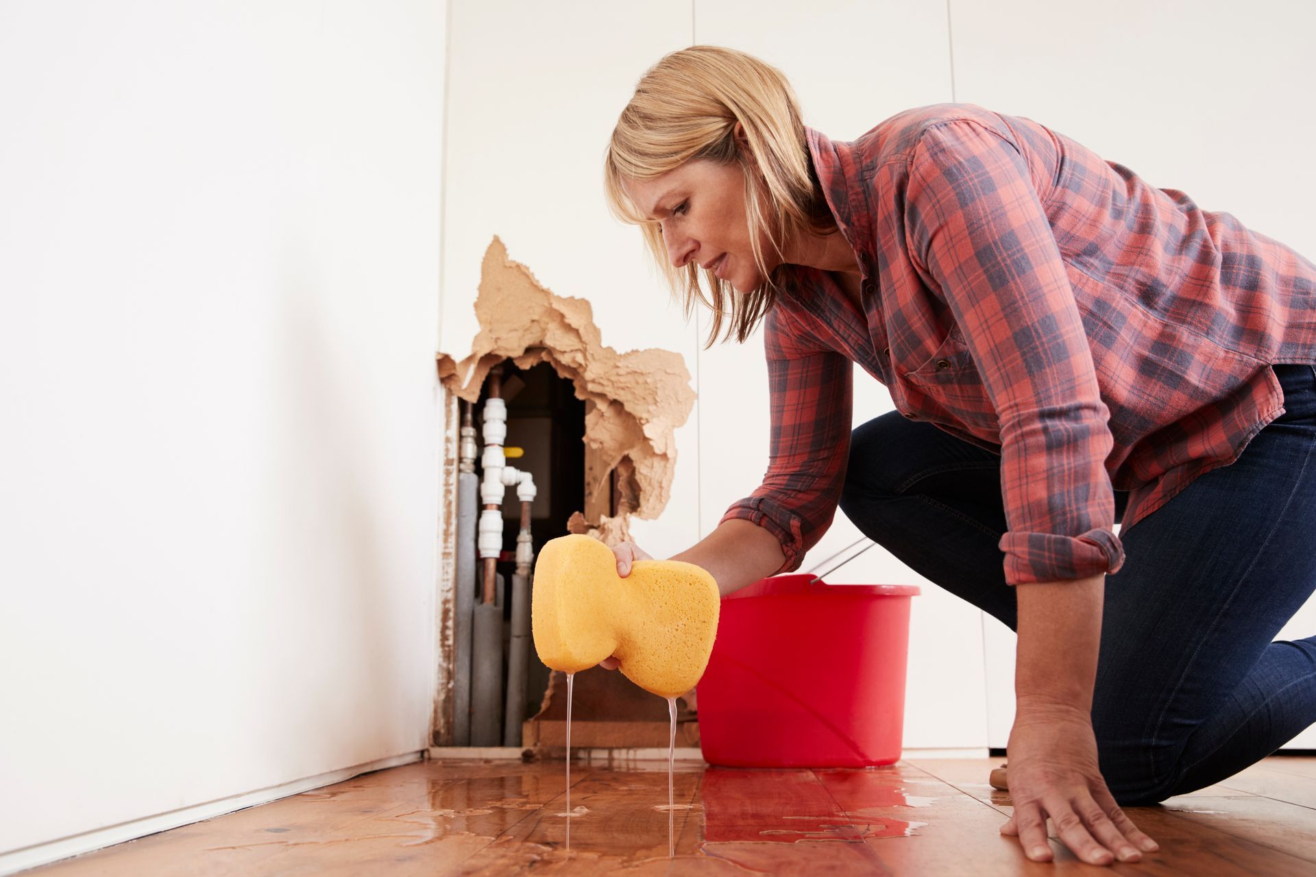 Worried homeowner mopping up water from a burst pipe with a sponge on a hardwood floor