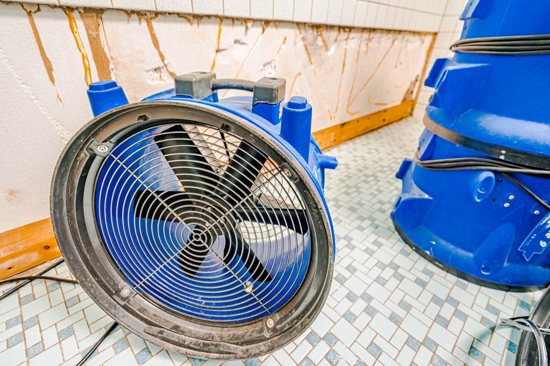 A blue industrial air mover drying a tile floor after water damage. A blue industrial air mover drying a tile floor after water damage.