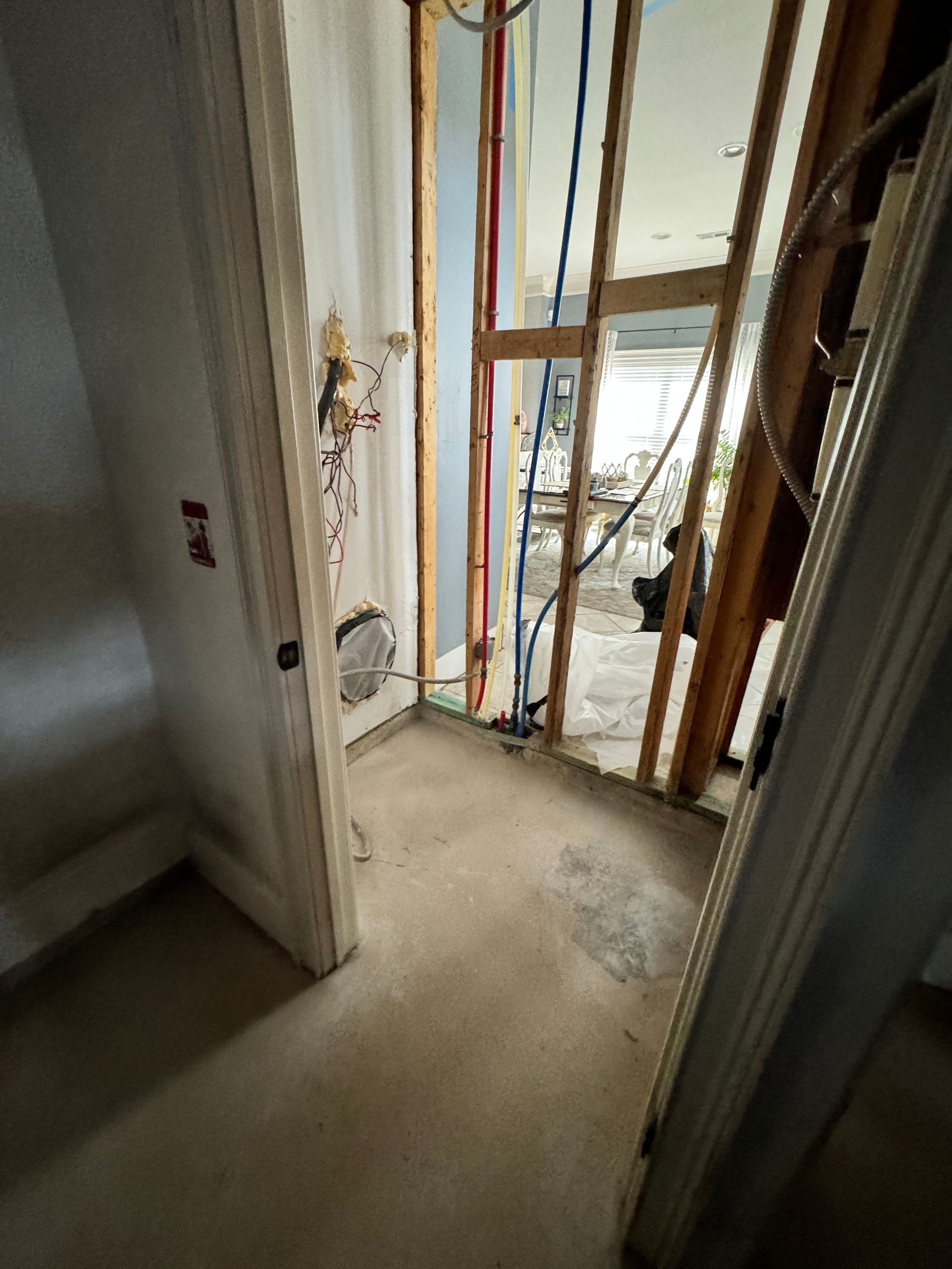 Interior view of a room under construction with exposed framing, pipes, and open doorway.