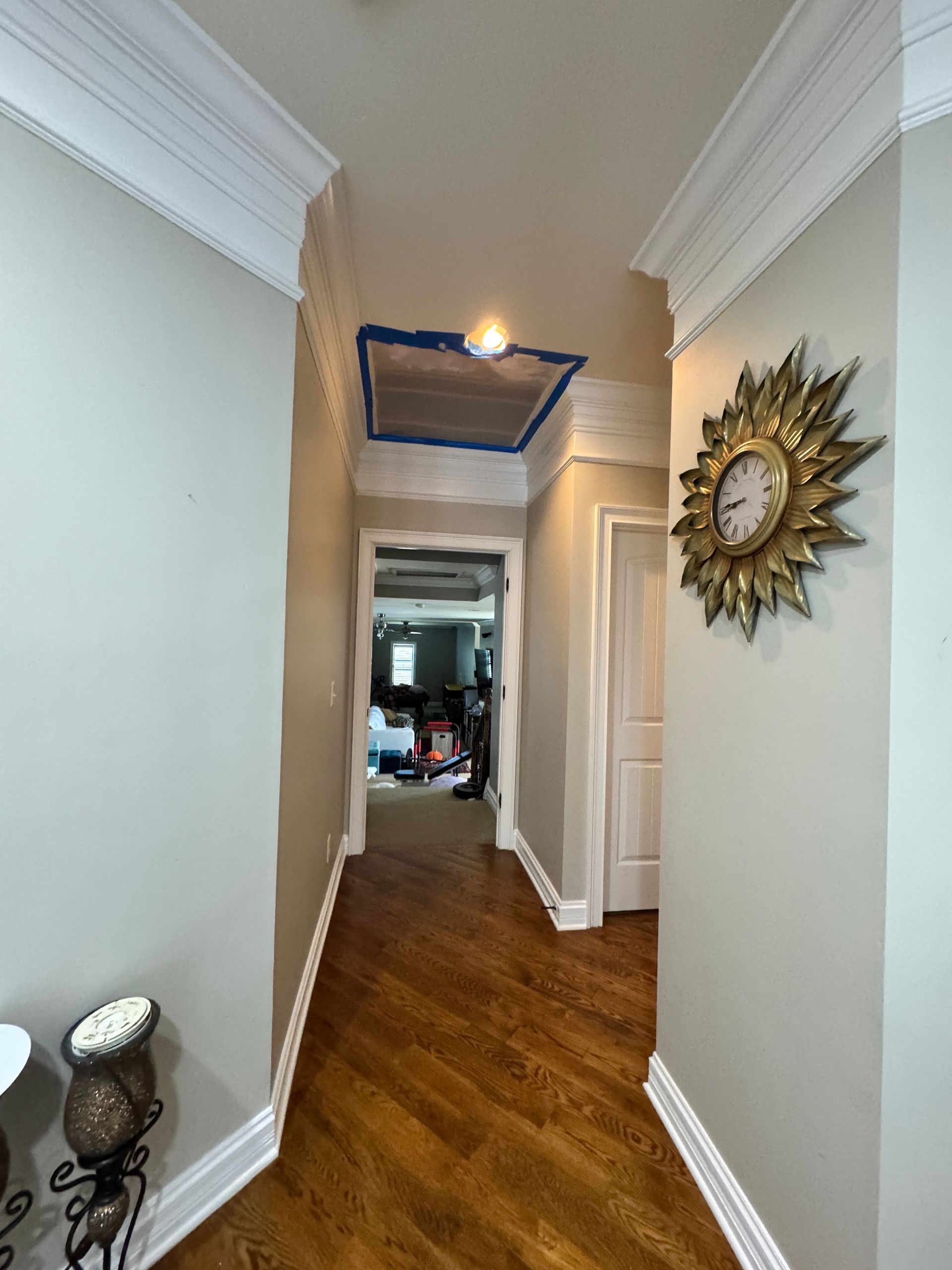 Narrow hallway with wood floor, white trim, and gold sunburst clock.
