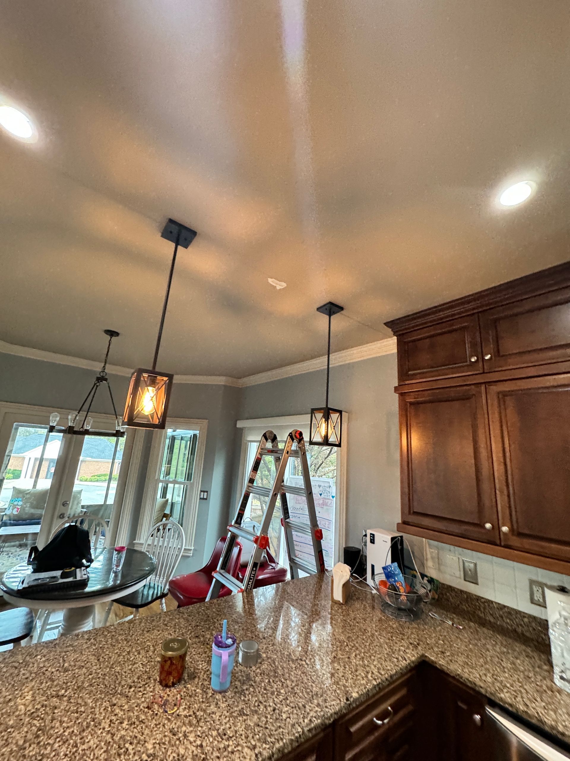 Kitchen with pendant lights, step ladder, and granite countertop. Cabinets on right.