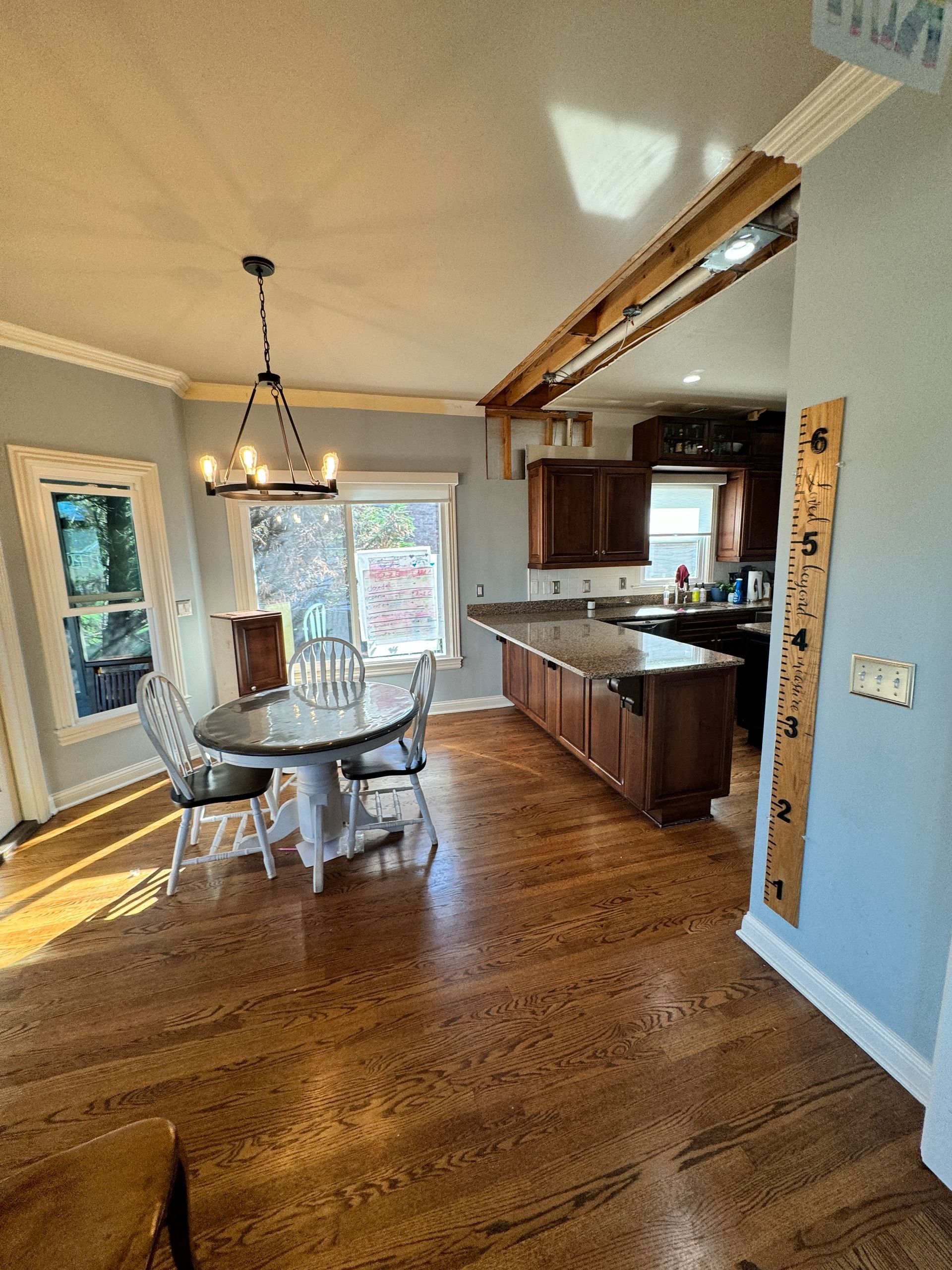 A dining room and kitchen with wood floors. Oval table with chairs, island with cabinets, light fixtures.