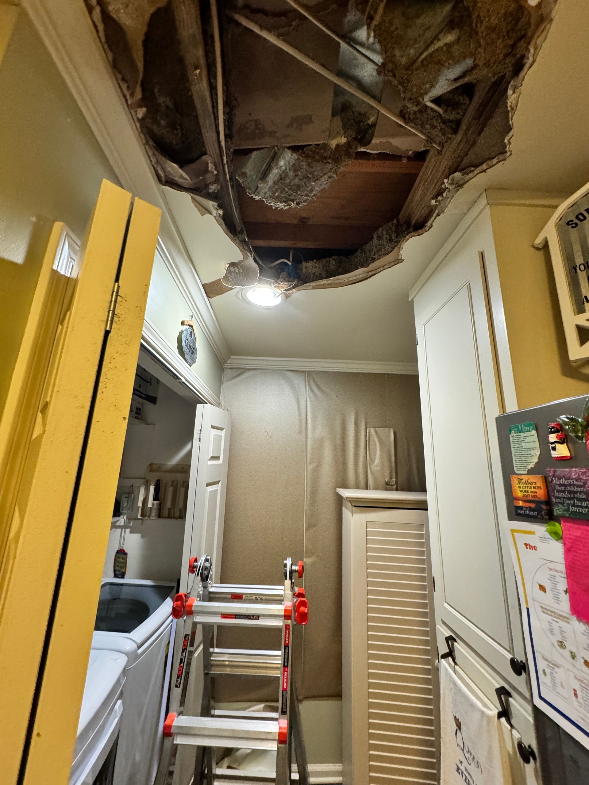 Damaged kitchen ceiling with a hole; a ladder stands below. Cabinets and appliances are visible.