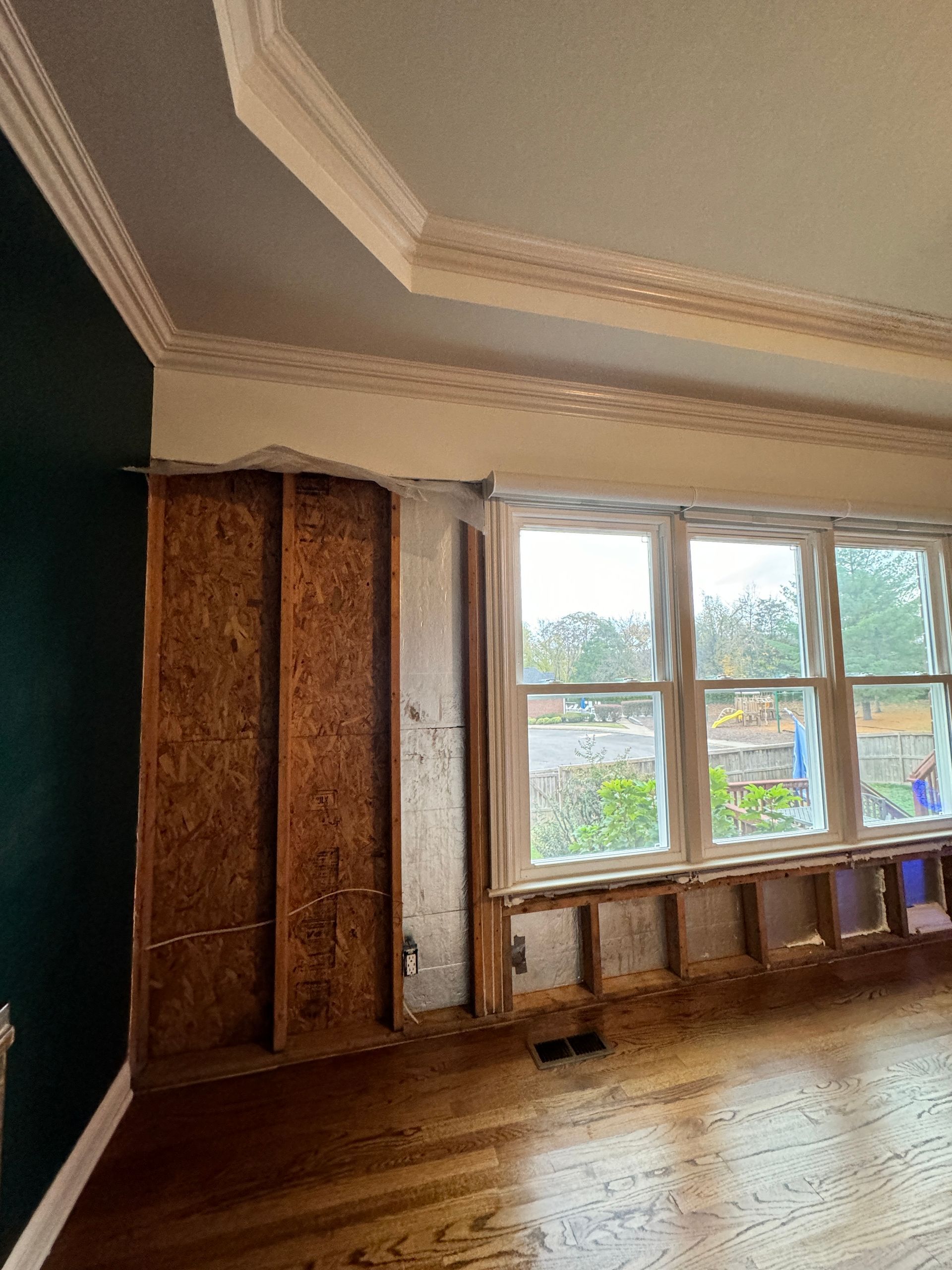 Interior view of room under construction with exposed wall studs, wooden floors, and a window.
