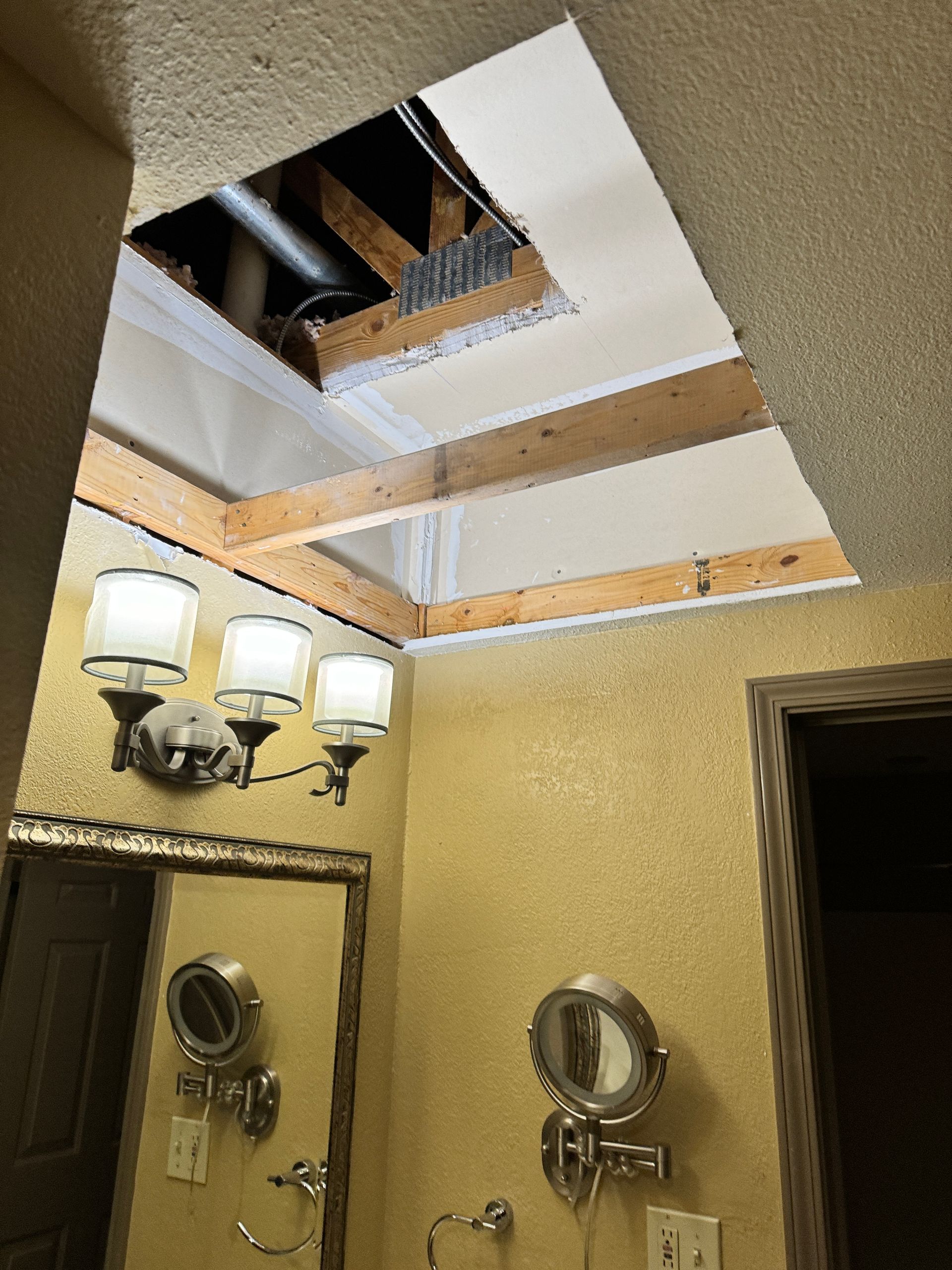 Bathroom with open ceiling, exposing attic. Light fixture, mirror, and yellow textured wall are visible.
