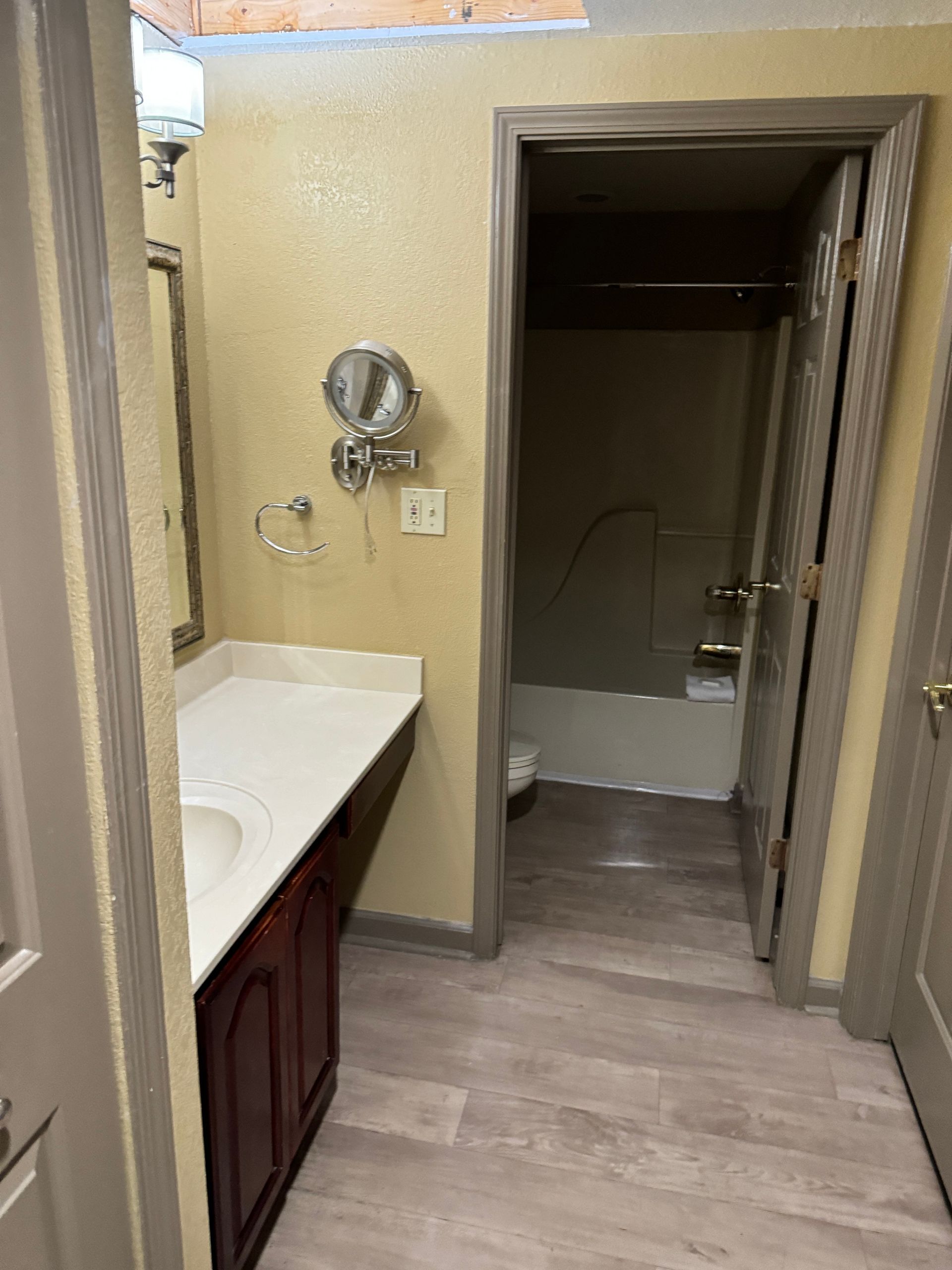 Bathroom with vanity, mirror, and doorway to a tub and shower. Beige walls, wood trim, gray flooring.