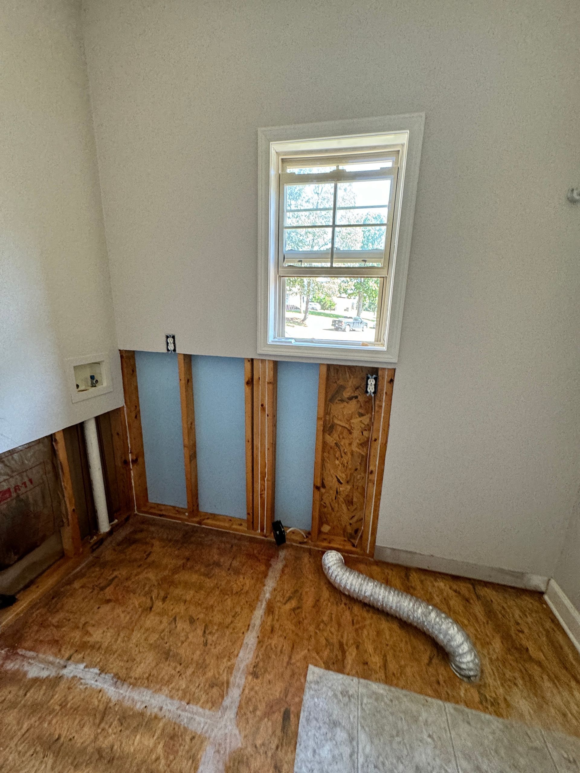 Laundry room with exposed wall studs, window, and ventilation pipe.