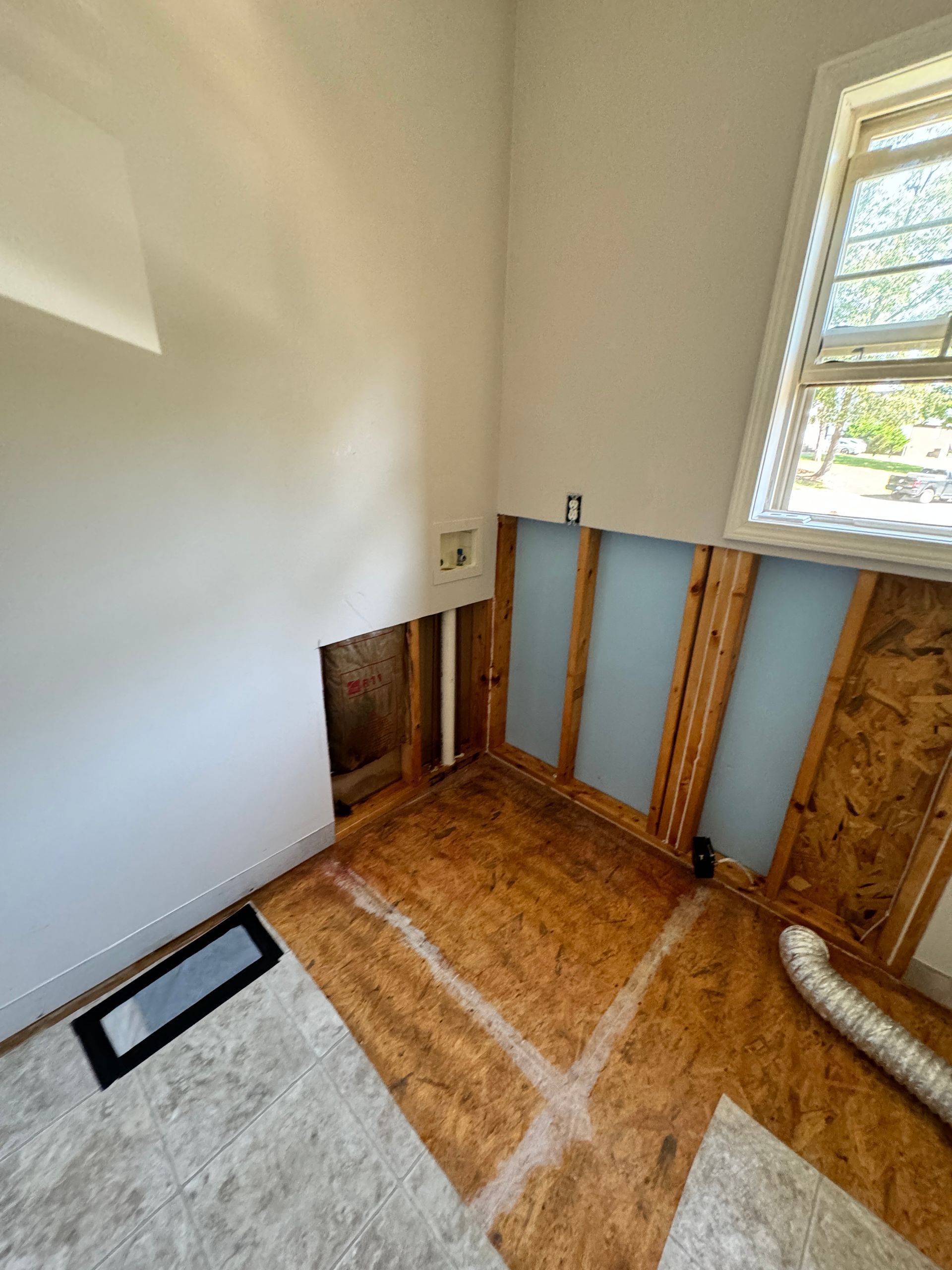Laundry room undergoing renovation. Exposed walls, unfinished flooring, open wall cavity, and a window.