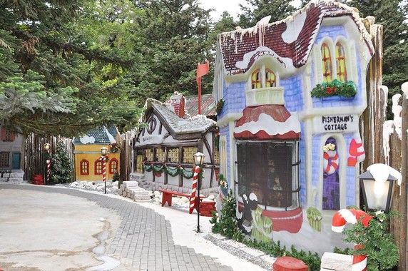 Uma fileira de pequenas casas decoradas para o Natal estão alinhadas em uma calçada.