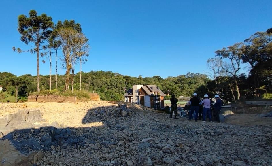 Um grupo de pessoas está em um campo de terra com árvores ao fundo.