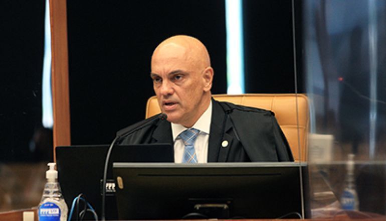 Um homem de terno e gravata está sentado em uma mesa em frente a um computador.