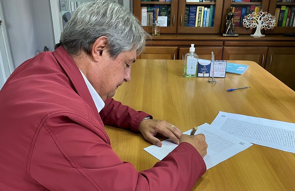 Um homem de jaqueta vermelha está sentado a uma mesa escrevendo em um pedaço de papel.