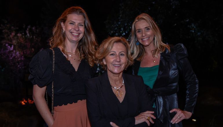 Três mulheres posam juntas para uma foto e sorriem.